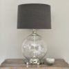 large glass ball shaped table lamp with chrome central pole, base and neck with a dark grey drum linen lampshade
