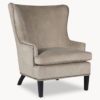 large armchair with a curved back upholstered in a warm champagne velvet with studed detail and wooden legs