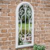 distressed white arched outdoor garden mirror with a decorative scroll design
