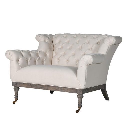 oversided large armchair loveseat upholstered in a cream linen with button back design and weathered wooden base with turned legs and castors at front
