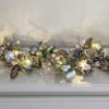 christmas light garland full of frosted pine cones, faux pine, berries, bark stars, silver baubles and warm white LED lights
