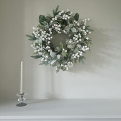 large artificial Christmas wreath made up with a full arrangement of mixed foliages in soft, muted green tones, dressed with delicate snowberries and lightly dusted with frosted snow and iridescent glitter for a subtle sparkle