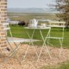 outdoor metal round table with two foldable bistro chairs with a light green painted finish