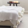 chunky knitted cream throw with large pom pom edges on two sides
