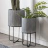 set of two round industrial style grey metal planters with a ribbed design set on a black framed stand