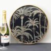 decorative round tray with built in handles in the rim with an antique gold painted finish and pearlescent palm tray black and gold glass tray base