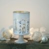 stemmed glass candle holder with a mottled white ocvering and cut-out winter design