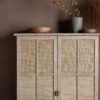 tall wooden cupboard on legs with internal shelving and two panelled doors with rattan detailing and metal handles