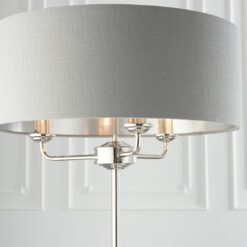 polished silver stemmed floor lamp with a three-arm light fitting and grey linen lampshade