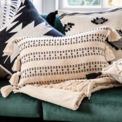 large rectangular cream cushion with a stitched black linear detailing and large cream pom pom edges