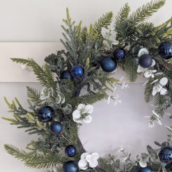faux pine and mixed foliage wreath attached to a sturdy round twig base and adorned with navy blue baubles and iridescent glitter